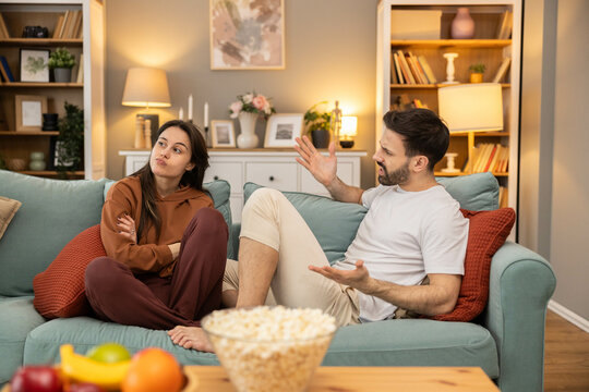 A couple engaged in a conversation on a sofa, showcasing expressions of disagreement and contemplation in a cozy living room.
