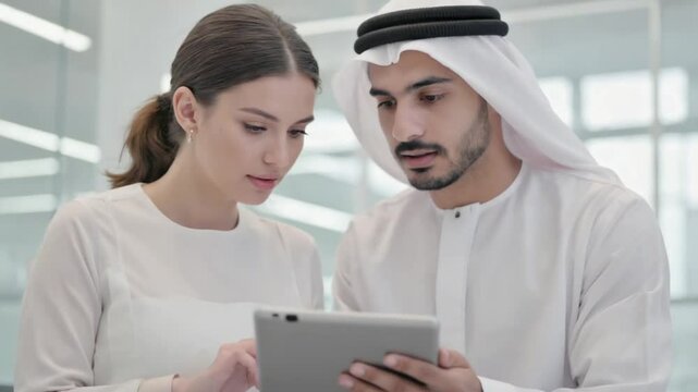 A woman and an Arabian man working on a tablet