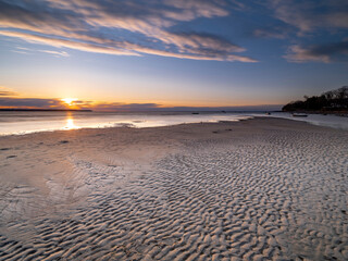 Fototapeta premium Sunset on rippled sandy beach with calm sea and colorful sky