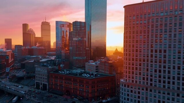 Distancing from the skyscrapers lit with pink light of sunset. Drone footage over the busy streets of Boston, Massachusetts, USA.