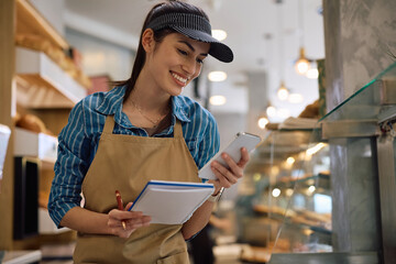 Happy woman using smart phone while working in bakery.