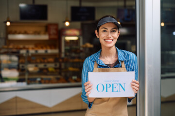 Happy female bakery owner holding open sign and looking at camera.