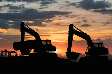 Crawler excavators silhouette are digging the soil in the construction site. With blue sky and clouds of on sunset background