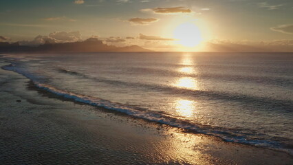 Golden hour sunlight reflects on the gentle ocean waves rolling onto a tropical beach at sunset, creating a serene and idyllic scene, perfect for a relaxing vacation getaway