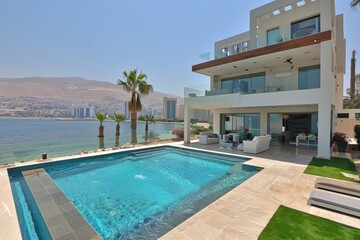 Fototapeta premium Modern villa with pool by the water and palm trees in a sunny location.