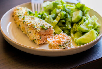 Close-up of a baked breaded salmon fillet served with a simple green salad in a dish. The salmon...