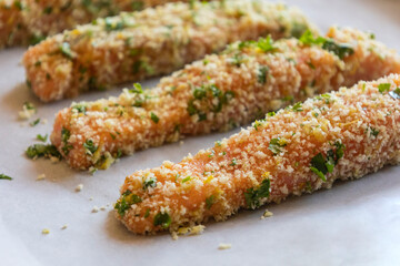 Close-up of raw breaded salmon fillets arranged in a tray, ready to be baked. The salmon is coated evenly with breadcrumbs, showing texture and freshness