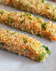 Close-up of raw breaded salmon fillets arranged in a tray, ready to be baked. The salmon is coated evenly with breadcrumbs, showing texture and freshness