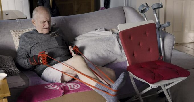 Exercise, legs and senior man with a band for fitness, workout and training on the sofa. Body, wellness and elderly person with rehabilitation after an injury in the living room during retirement