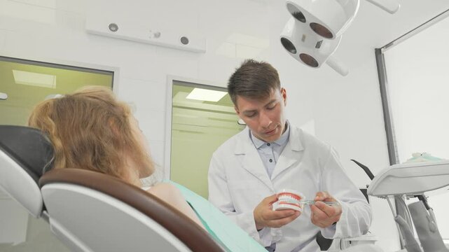 Young male dentist demonstrating proper tooth brushing techniques on a dental model