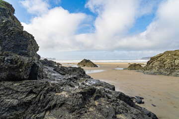 Paysage côtier de la presqu'île de Crozon, contrastes entre les rochers noirs, le sable clair et un ciel nuancé de bleu et de blanc.