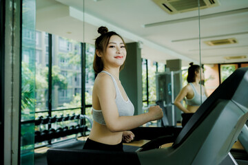 Obraz premium A young woman enjoys a light cardio jog on the treadmill at the gym, headphones on and music playing as she stays focused and relaxed.