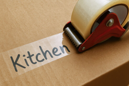 Packing tape on cardboard box labeled kitchen ready for moving or eviction notice while managing debt during relocation or storage