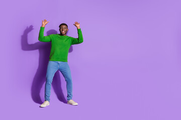 Young man in green sweater on purple background expressing joy with energetic gestures of happiness...