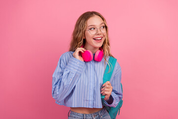 Young woman with a trendy style wearing glasses and headphones holding a backpack against a bright...