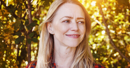 Nature, happy and woman by trees with sunshine for wellness, fresh air and relax outdoors. Countryside, smile and person in forest, woods and morning for calm, joy and freedom in natural environment