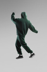 Individual wearing dark green sportswear performs dance moves against a neutral background during...