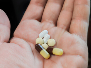 A hand holding colorful capsules and pills is depicted on a blurred background.