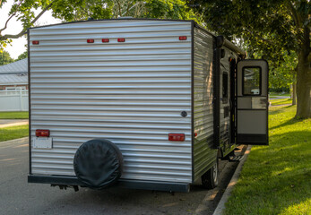 Rear view of a camping trailer with an open door parked on the road in a residential neighbourhood