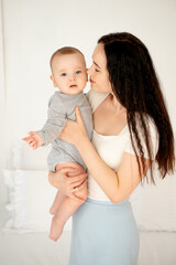 mom and baby, mother hugs and kisses baby holding him in her arms, maternal love and care, young mom having fun with baby baby, mom's decree