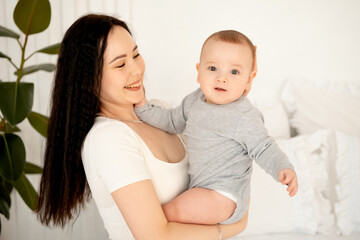 mom and baby, mother hugs and kisses baby holding him in her arms, maternal love and care, young mom having fun with baby baby, mom's decree