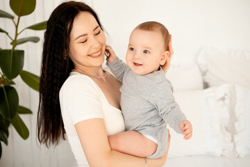 mom and baby, mother hugs and kisses baby holding him in her arms, maternal love and care, young mom having fun with baby baby, mom's decree