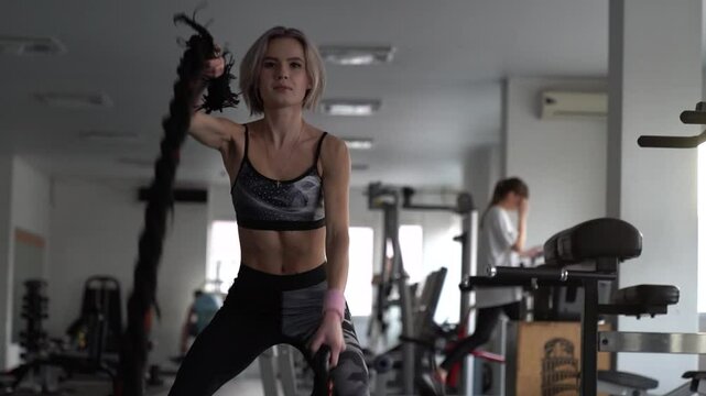 sstkWellness , Athletic girl focused on fitness training with ropes at gym, Sport. Attractive young fit sportswoman working out in functional training gym doing exercise with battle ropes.