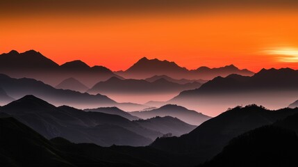 Fototapeta premium Layered mountain ranges are silhouetted against a vibrant orange sunset sky