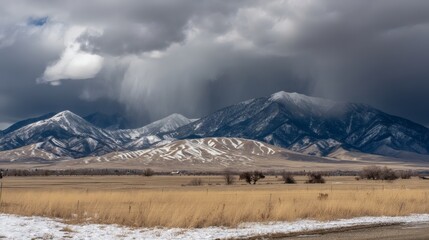 Dramatic Mountain Landscape Reveals Approaching Winter Storm With Snowfall Covering Peaks Highlighting The Contrast Between The Golden Field And Dark Sky