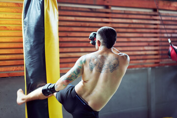Shirtless athlete kicking a heavy bag during a boxing training session in a gym