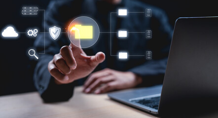 Businessman interacts with a virtual folder icon on a digital interface next to a laptop, symbolizing data management and technology.