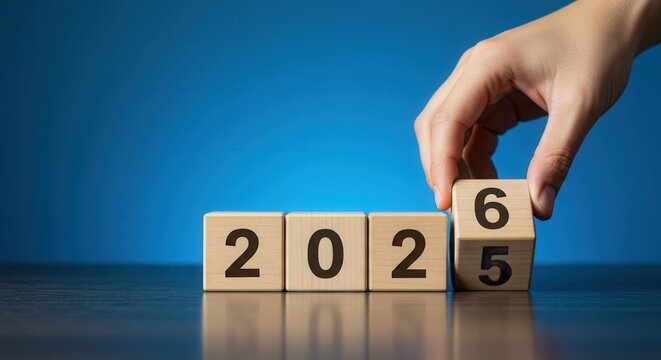 Hand placing a wooden block with number 6 to change year 2025 to 2026 on a blue background.