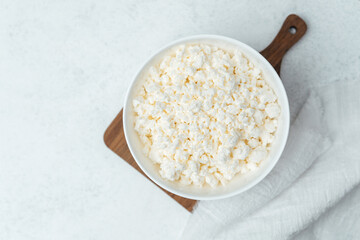 Creamy cottage cheese in a bowl on a wooden board in a bright kitchen