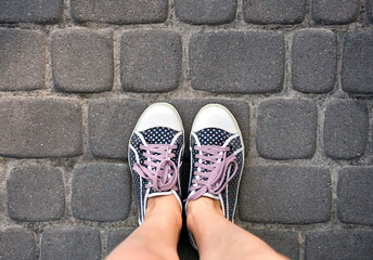 Woman's legs in polka dot sneakers on the stone road. Top view. Copy space.