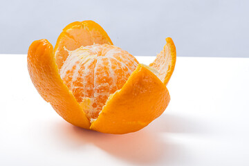 Partially peeled orange fruit placed on clean white surface with bright background, showing juicy segmented texture, vibrant color, and natural freshness of tropical citrus fruit