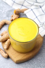 Tasty turmeric latte in cup and roots on grey table, closeup