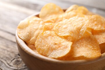 Tasty potato chips in bowl on wooden table, closeup
