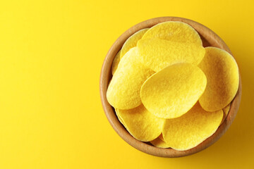 Tasty potato chips in bowl on yellow background, top view. Space for text