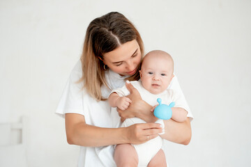 mom and baby, mother hold a newborn baby in her arms at home in the bedroom, hugging him, playing with him with a rattle, maternal care and love, portrait of a happy mother with a child.