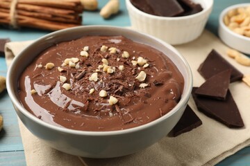 Tasty chocolate pudding in bowl and ingredients on light blue wooden table, closeup