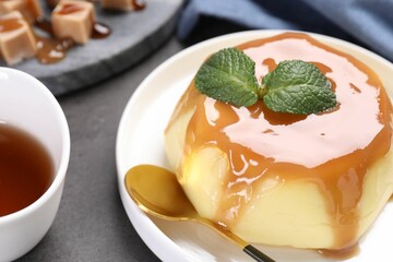 Delicious pudding with caramel sauce and mint served on gray table, closeup