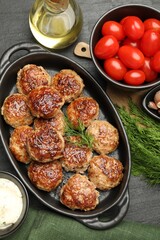 Delicious patties in baking dish, spices and tomatoes on black table, flat lay