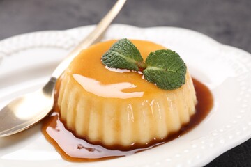 Delicious pudding with caramel sauce and mint served on gray table, closeup