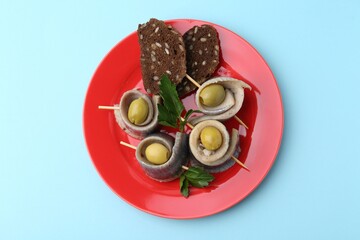 Delicious herring rolls with olives, parsley and bread on light blue background, top view