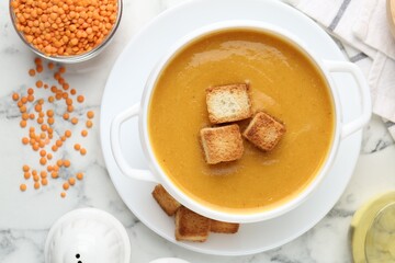 Delicious lentil cream soup served with croutons on white marble table, flat lay