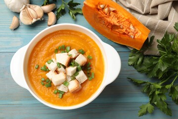 Tasty pumpkin cream soup with croutons, green onion, garlic and parsley on light blue wooden table,...