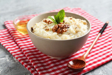 Delicious rice pudding with walnuts, mint, honey and spoon on grey table, closeup