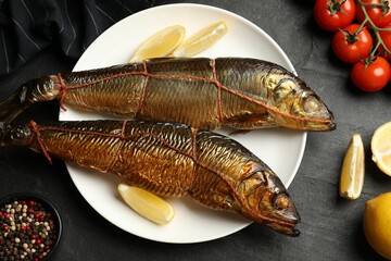 Delicious smoked herrings with lemon slices and other products on black table, flat lay