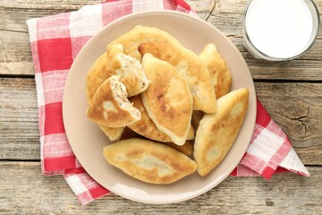 Delicious fried pyrizhky (stuffed pies) and milk on wooden table, top view
