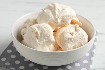Delicious homemade meringue cookies in bowl on light table, closeup